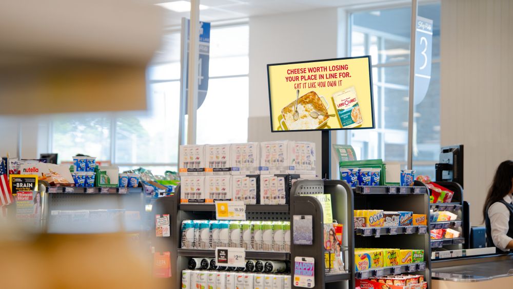 A shopper at a sanitizer stand with a digital screen running a nutrition-bar campaign.