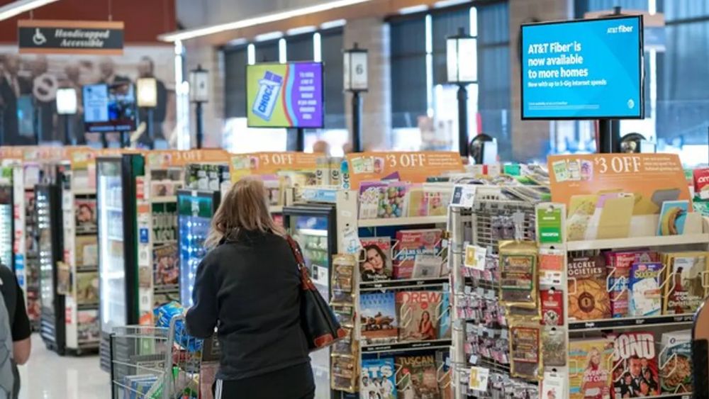 Overhead digital screens above the front-end aisles, alongside coupon and magazine racks.